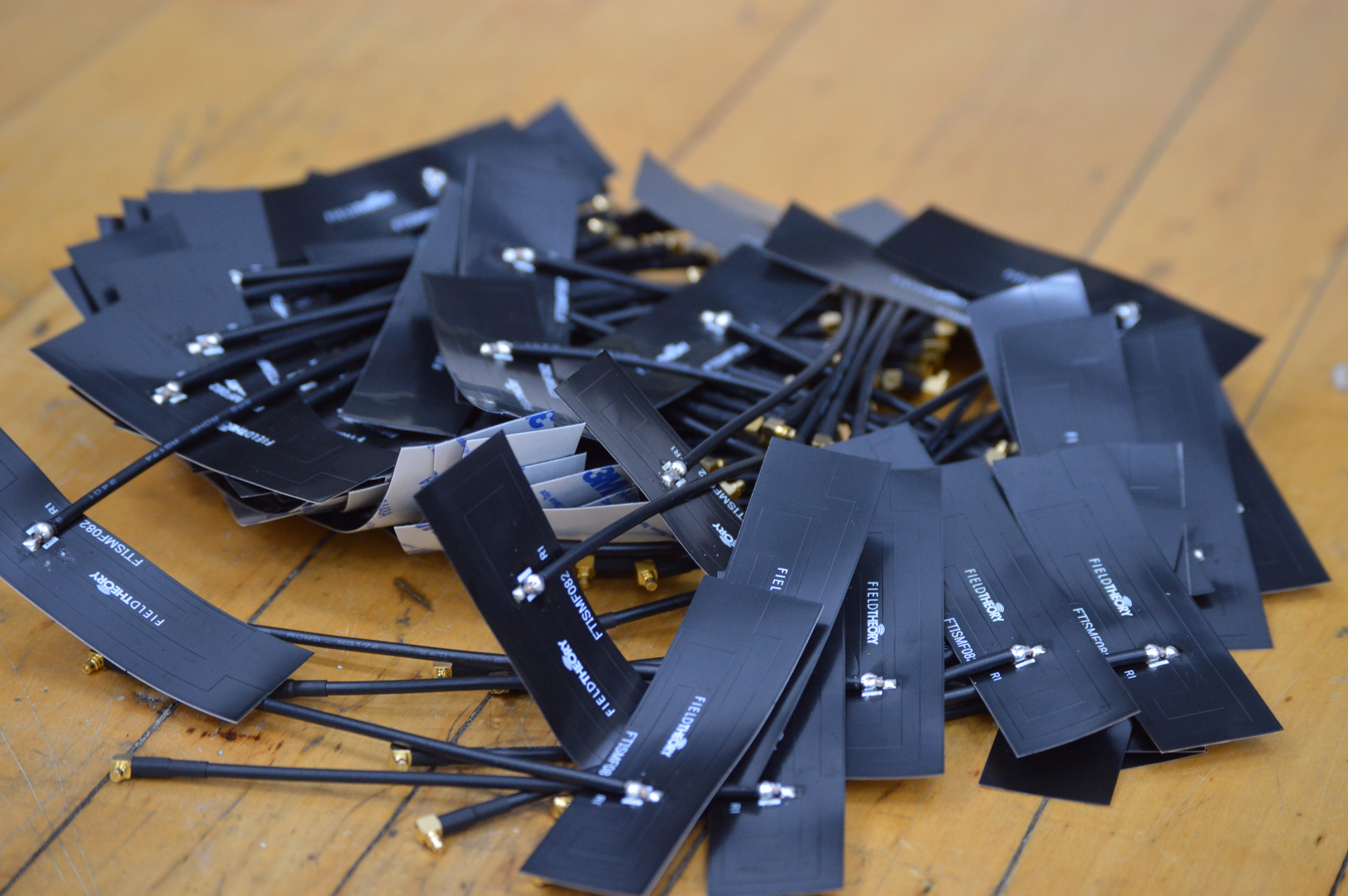 Pile of small adhesive antennas on wooden table, each branded with the Field Theory logo