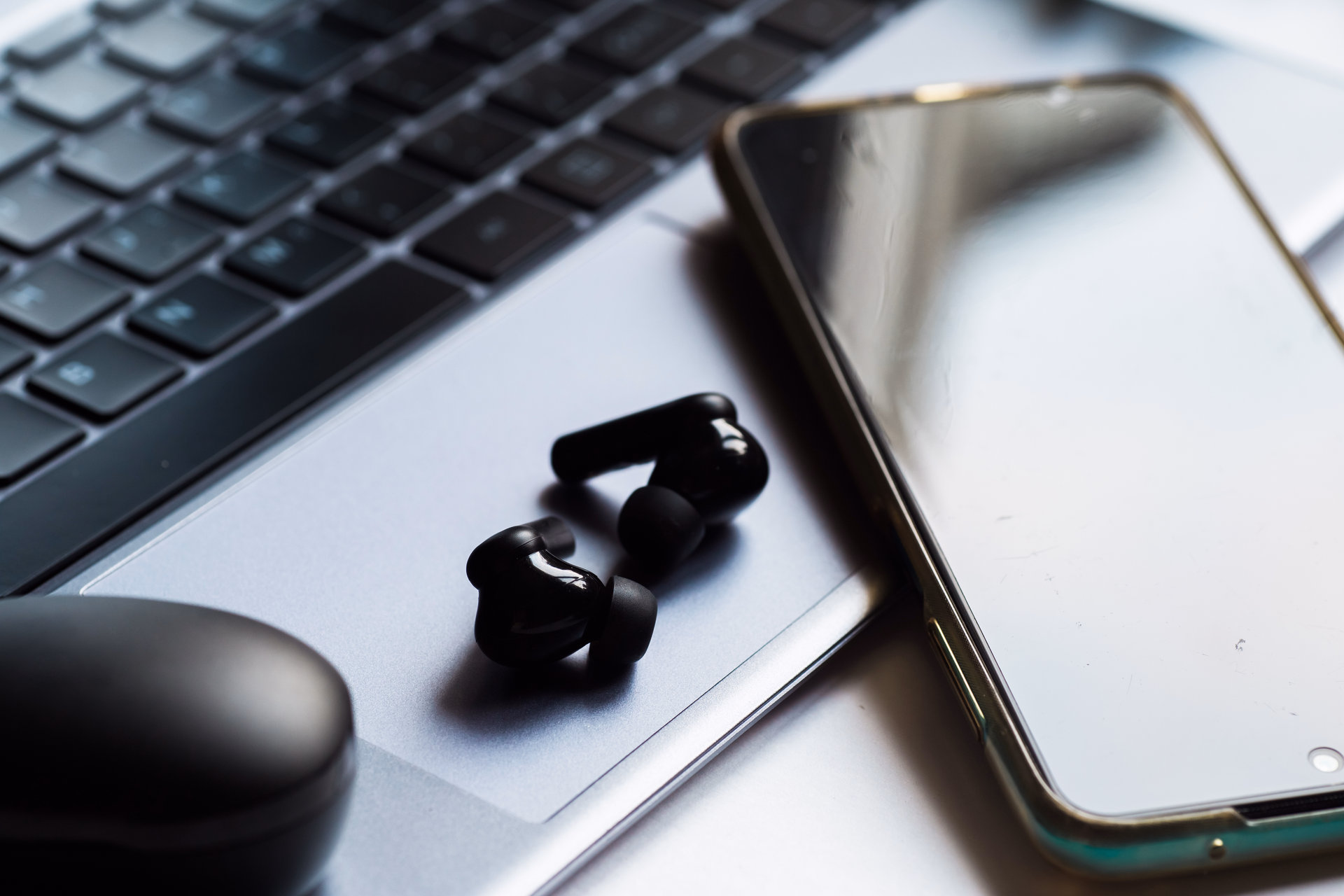 Wireless headphones and smartphone sitting on top of laptop keyboard